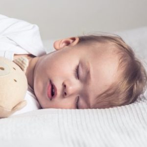 Sleeping baby in his crib, holding a teddy bear.